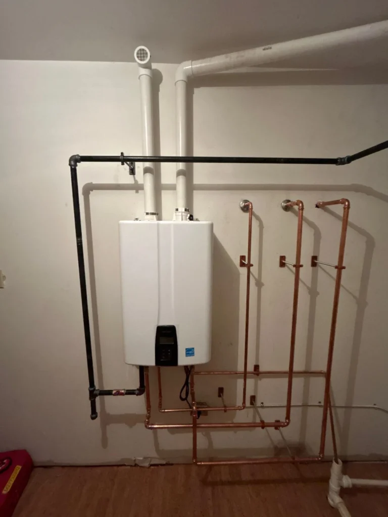 Navien tankless water heater mounted on a wall in a historic Nashville home, with a copper manifold, twin vents and a black iron gas line
