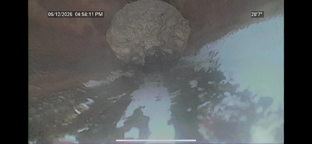 Camera footage from inside a drain line, showing the pipe wall and standing water