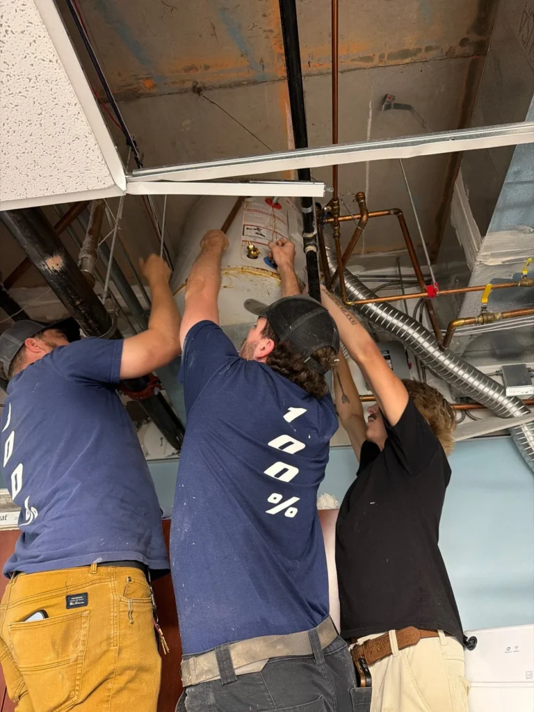 Two 100 Percent Plumbing technicians working above a ceiling grid on a commercial water heater replacement in Mount Juliet