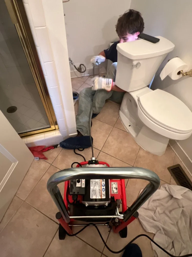 Technician running a drain machine at a pulled toilet in a Nashville bathroom