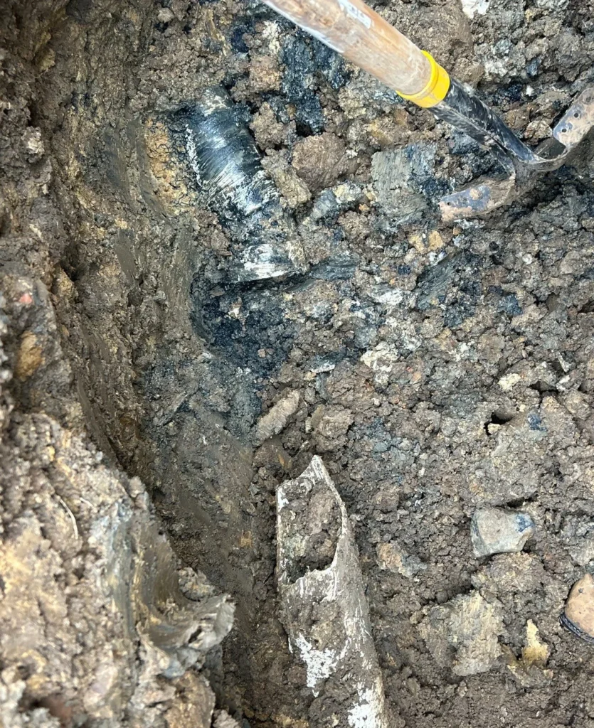 Old drain line exposed in rock before replacement in Forest Hills
