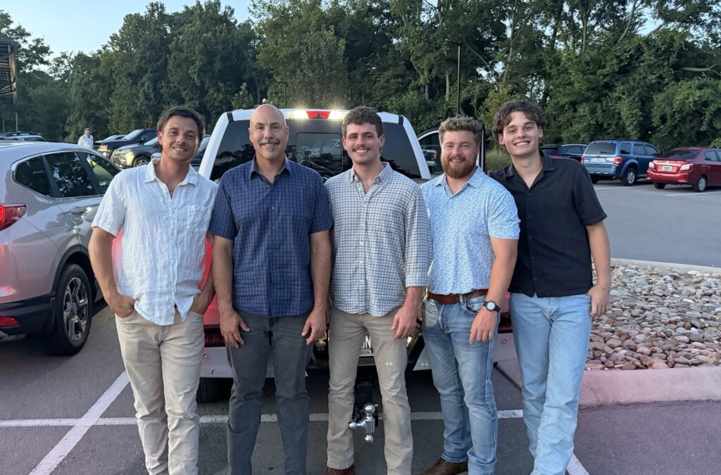 Five 100 Percent Plumbing technicians standing together outside their truck at the end of a workday in Nashville